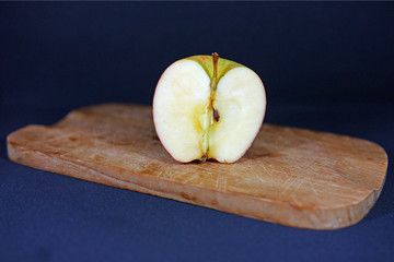 Red apple cut into half on a wooden board with black background showing a half inner part