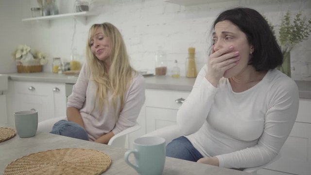 Ault Caucasian women sitting at the table in the morning with coffee cups and yawning. Exhausted female friends waking up after hanging out. Friendship, leisure, lifestyle.