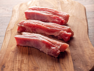 Three raw pork belly slices on a wooden cutting board, Dark wood table surface.