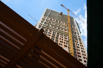 Fototapeta premium Construction site of the high skyscraper building. Building activity of modern residential building. Yellow crane machinery from low angle view. Kyiv, Ukraine.