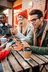 Happy friends holding their smartphones in street cafe