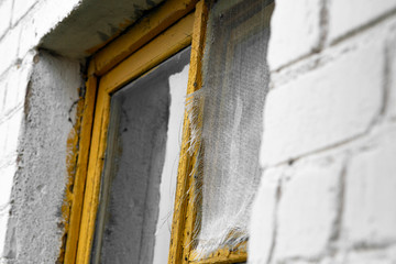 Fragment of an old yellow wooden window in a white brick house with a grid on the window leaf, closeup