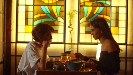 Two girls sit at a table in a cafe and talk