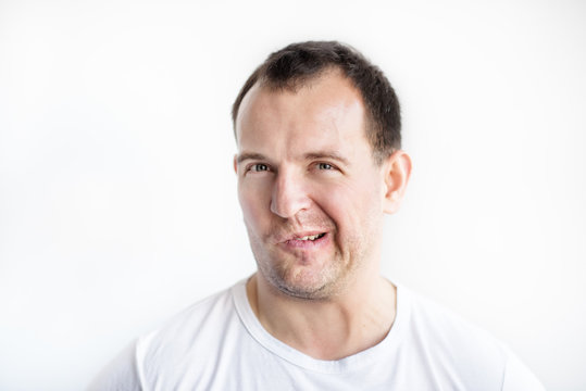 Closeup portrait of disgusted 30 years old caucasian white man on white background in white t-shirt. Man making weird face and looking in camera. Afraid, desperate, disgusted guy conceptual picture.