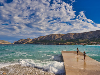 Children on the marina of a blue sea, illuminated mountains and intense sky with clouds