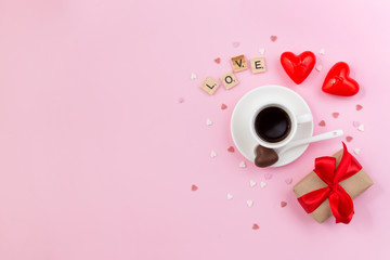 Valentine's day. Pink background with cup of coffee, gift box and candles. Love made of wooden letters