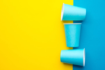 Blue paper disposable cups yellow and blue background. Cooking utensil. Cutlery sign. Top view. Minimalist Style. Copy, empty space for text