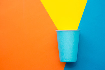 Blue paper disposable cup on beautiful multicolored background. Top view. Minimalist Style. Copy, empty space for text