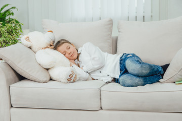 Sweet charming kid is lovely sleeping on her big white teddy-bear. Full-length.