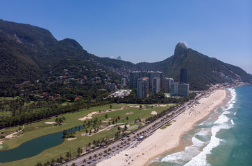 Aerial panorama of coastal S&atilde;o Conrado golf course with beach in the foreground and Two Brothers mountain and Corcovado mountain behind shantytown Rocinha in the background against a blue sky