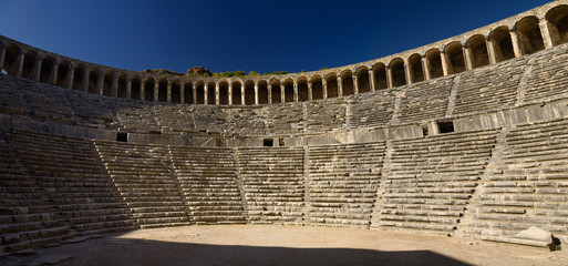 Panorama of semicircular stone seats at Aspendos Amphitheatre with upper gallery arches and stage...