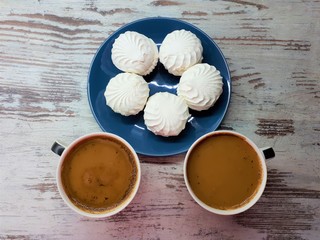 close-up of large cups with coffee / cocoa and white marshmallows on a blue plate on a background of abstract wooden surface