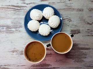 close-up of large cups with coffee / cocoa and white marshmallows on a blue plate on a background of abstract wooden surface