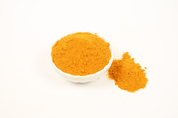 Turmeric powder in a white cup and a pile of turmeric powder on a white background