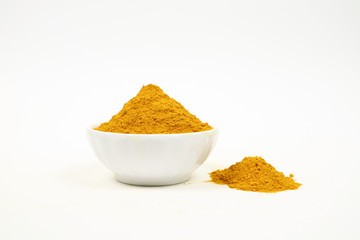 Turmeric powder in a white cup and a pile of turmeric powder on a white background