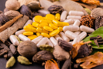 herbal medicines concept. Close up of yellow capsules and tablets with dry herbs on a black background