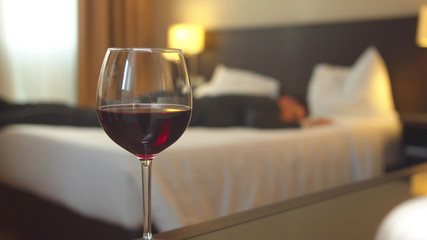 Focus on glass of wine in room of the hotel, man in suit sleep on the bed