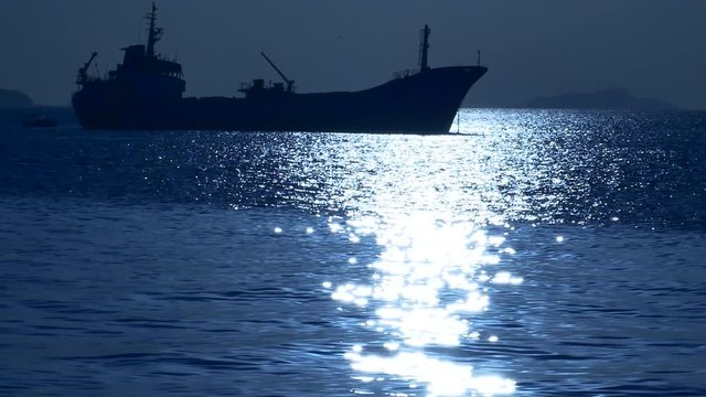 Cargo ship silhouette in the moonlight reflected on the water. Freighter floating in the ocean on a moon light night background. Recorded at 30fps, Camera Original Codec Cinelike D, priority to high d