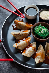 Close-up of pan fried gyoza dumplings with seaweed salad, sesame and soy sauce, vertical shot, selective focus