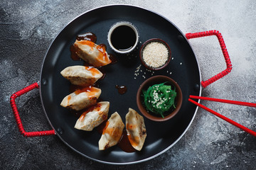 Serving pan with japanese gyoza dumplings, flatlay over dark-grey stone background, horizontal shot