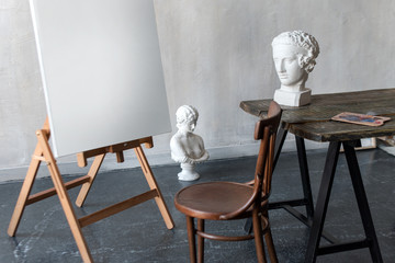 Sculptures of woman head at artist working place in the old atmospheric studio. Gypsum plaster sculptures and blank canvas