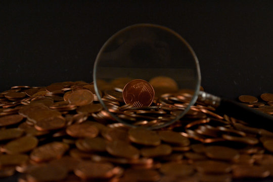 Magnifying glass on a heap of coins against black background