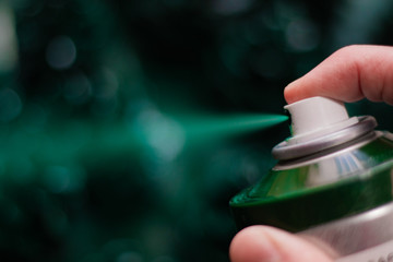 Green spray paint. Green spray from a spray can. Blurred turquoise background. A finger presses on...