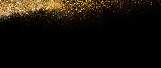 Wide view of a golden glitter scattered on a black surface. Christmas, new year, birthday, special occasions background, with a copy space.