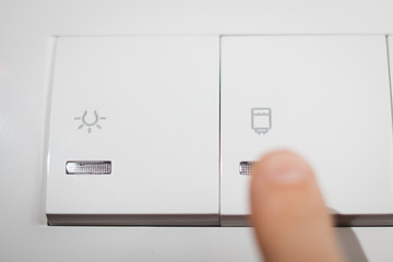 White double switch, controls light and water heater, close up shot. Finger pressing switch.
