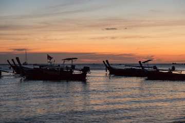 Silhouette group of traditional long tail boats floating in the sea with twilight of sunset in background