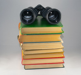 Binoculars directed by lenses on the audience lies on a stack of old multi-colored books on a white...