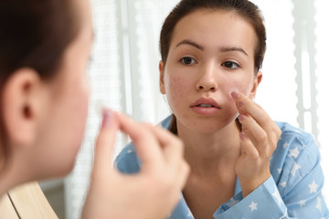 Teen girl applying acne healing patch near mirror in bathroom