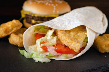 fast food roll with chicken and vegetables, burger with beef and chicken nuggets on a stone board on a wooden background