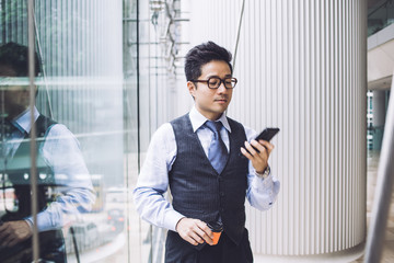 Pensive Asian businessman using smartphone in hall