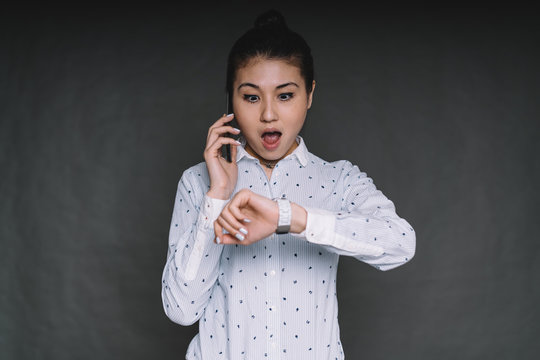 Surprised Asian woman checking time talking on smartphone