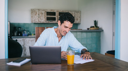 Cheerful man working with laptop and documents at home