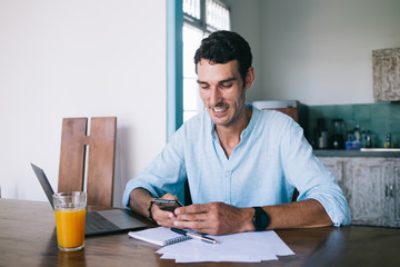 Happy male freelancer using phone at table