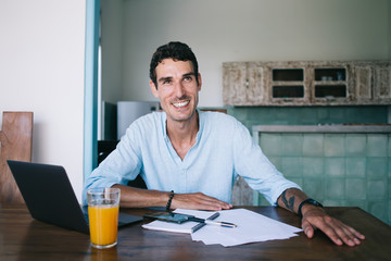 Cheerful adult male employee sitting at table during work