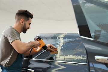 Worker tinting car window with heat gun in workshop