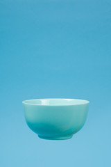 A blue ceramic mattle deep bowl for breakfast flying on blue background.