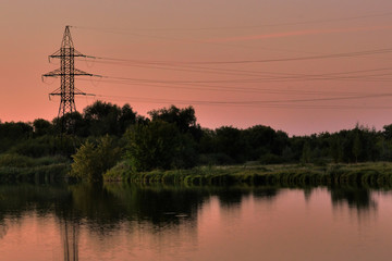 The power transmission tower are visible on the lake in the evening.  now time. Background for the energy industry. Beautiful background. Toned. Wires are visible in the sky in the evening.
