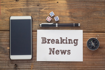 Breaking News Words written on white on wooden desk with dice,compass,smart phone and pen.Top view conceptual