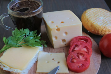Cheese with tomatoes and coffee lies on a wooden board on a brown table	