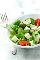 Healthy salad with feta chesse, green olives, cherry tomatoes and fresh herbs. Bright wooden background. Close up. 