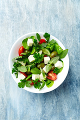 Healthy salad with feta chesse, green olives, cherry tomatoes and fresh herbs. Wooden background. Top view.