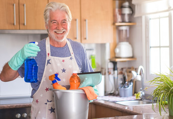 A senior smiling man ready to start housework. He holds a plastic bucket with cleaning items inside...