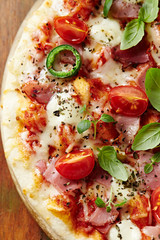Pizza with ham, cherry tomatoes, mozzarella cheese, jalapeno pepper and fresh herbs. Top view. Close up. 