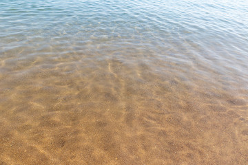 Soft wave of turquoise sea water on the sandy beach. Close-up.