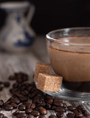 Glass cup with coffee with milk, latte coffee. A jug of milk in the background. Cane sugar on a saucer. Coffee beans on a wooden background. Close-up. Vertical orientation.