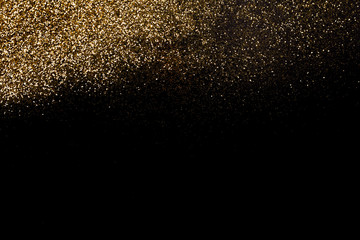 Fototapeta na wymiar Golden glitter dispersed on a deep black surface. Christmas, new year, birthday, special occasions background, with a copy space.